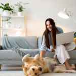 happy dog in a home rental with a girl sitting on a couch with laptop in one hand.